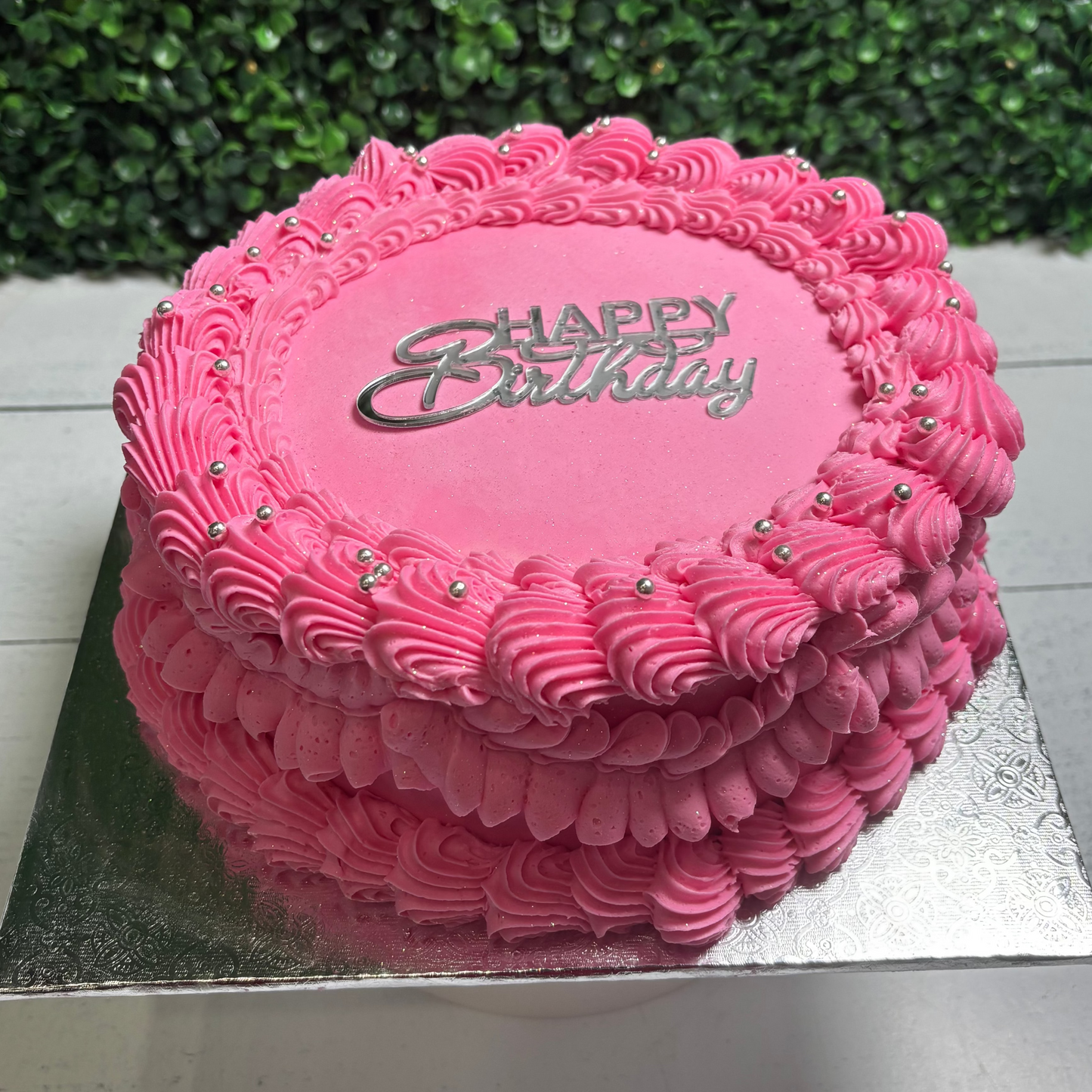 Pink vintage style birthday cake with 'Happy Birthday' text on a green outdoor background