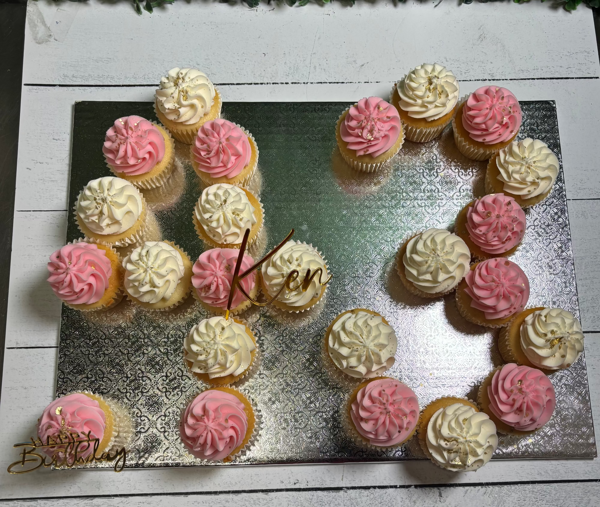 Cupcakes arranged to form the number '25' with pink and white frosting on a metallic surface.