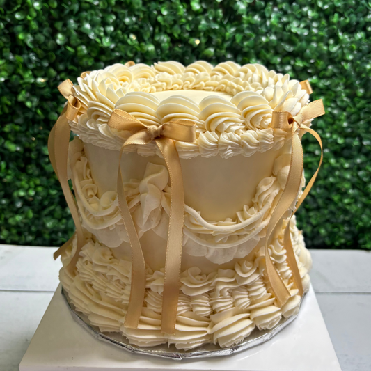 Ivory vintage sytled cake  with ruffled details and ribbons against a green leafy background
