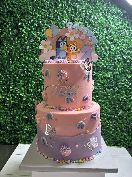 Three-tiered birthday cake with cartoon character Bluey topper against a green leafy background