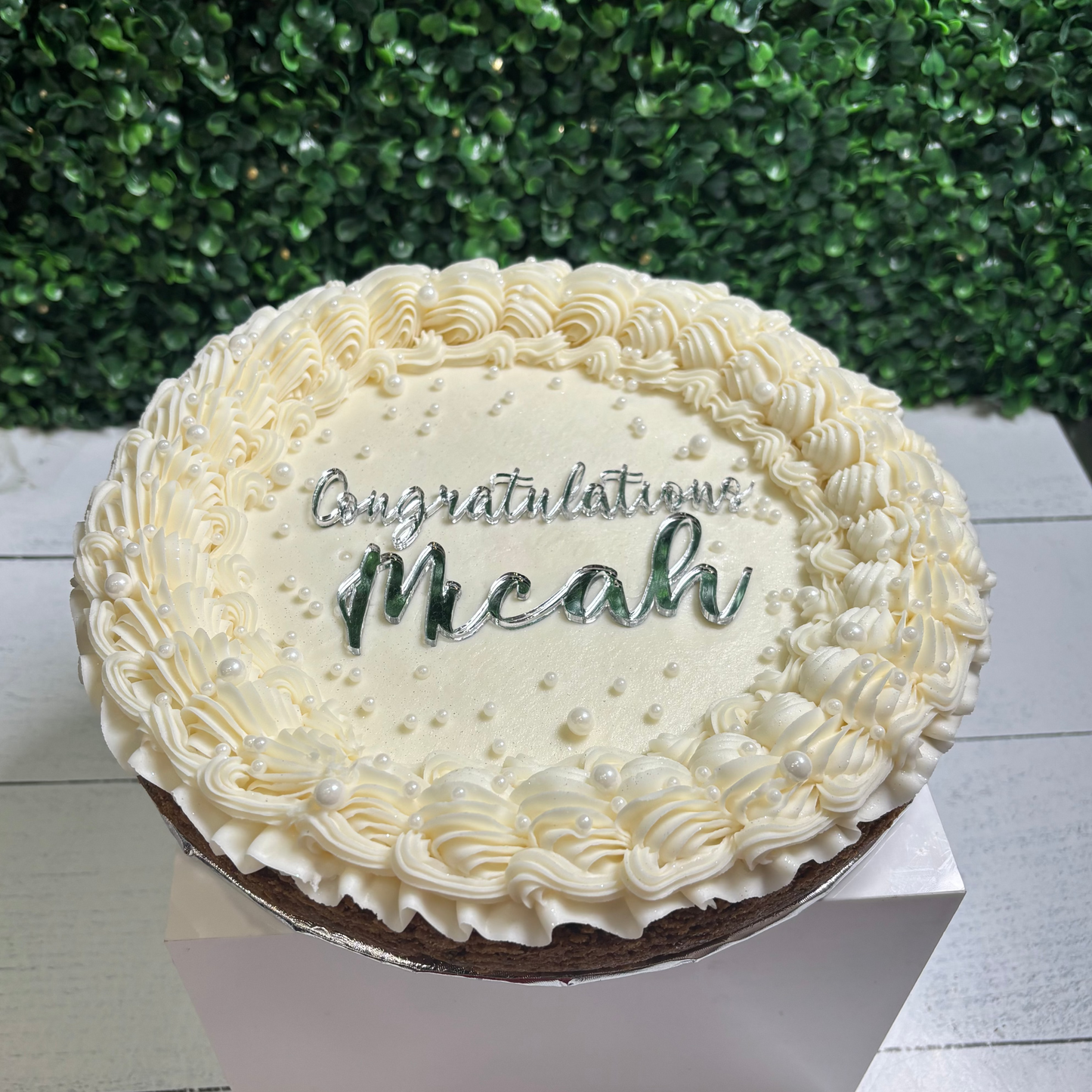 Decorative cake with 'Congratulations Meahu' text against a green bush background
