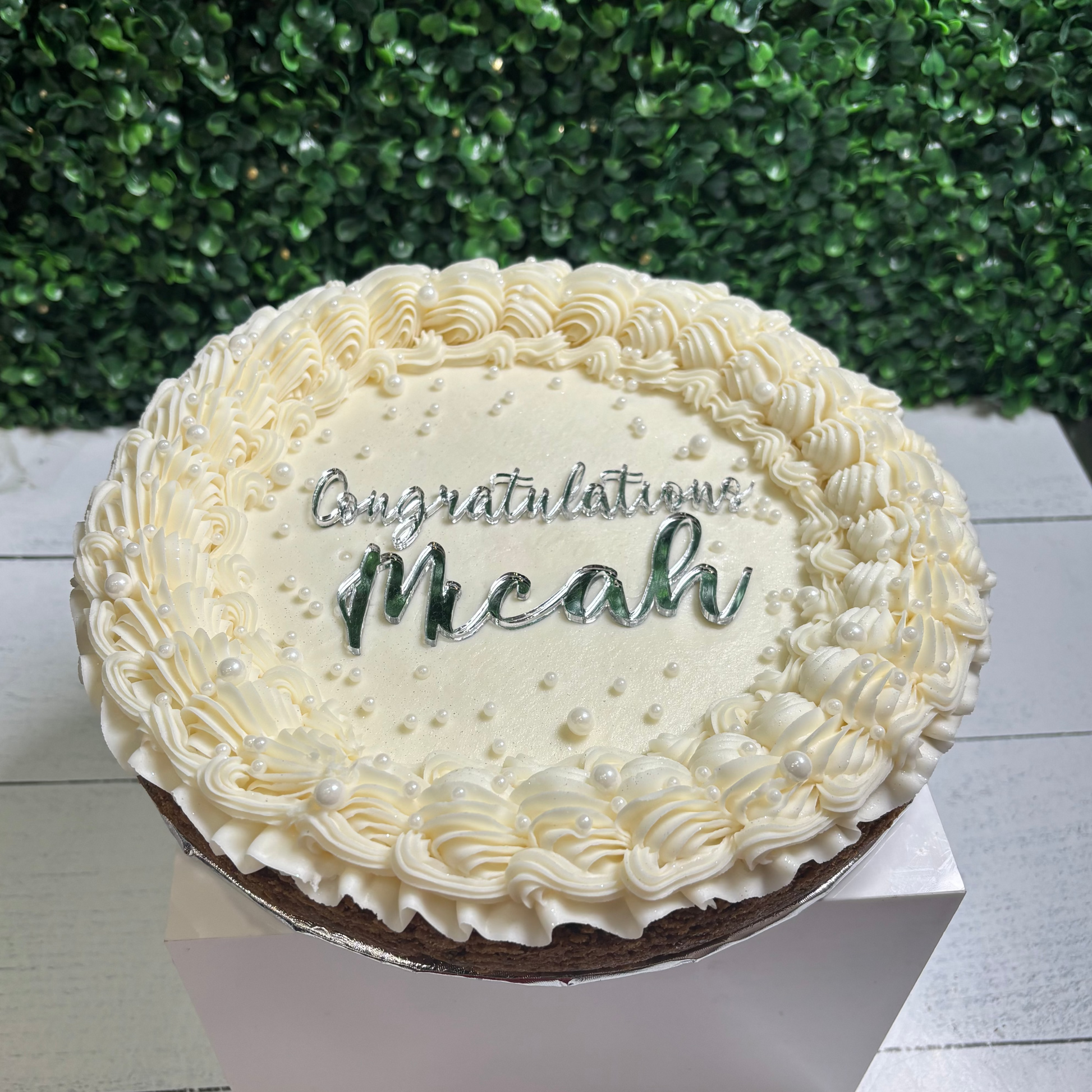 Decorative cake with 'Congratulations Meahu' text against a green bush background